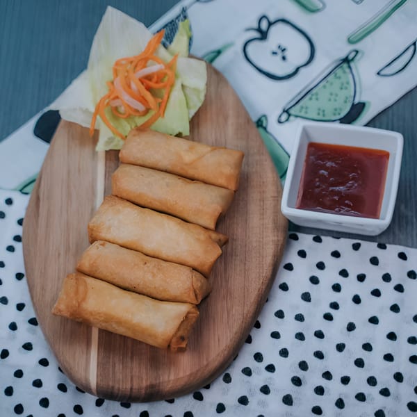 Crispy Vietnamese spring rolls on a wooden board with lettuce, shredded carrots, and dipping sauce.