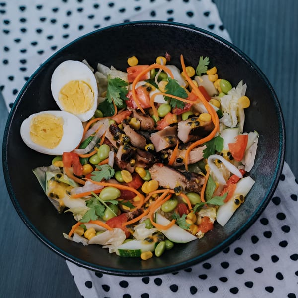 Vietnamese fusion salad with chicken, vegetables, passion fruit, and hard-boiled eggs in a black bowl.
