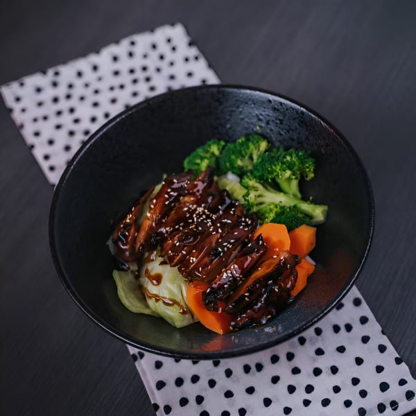 Green Mint Vietnamese Fusion's teriyaki chicken with broccoli, carrots, and cabbage in a black bowl.
