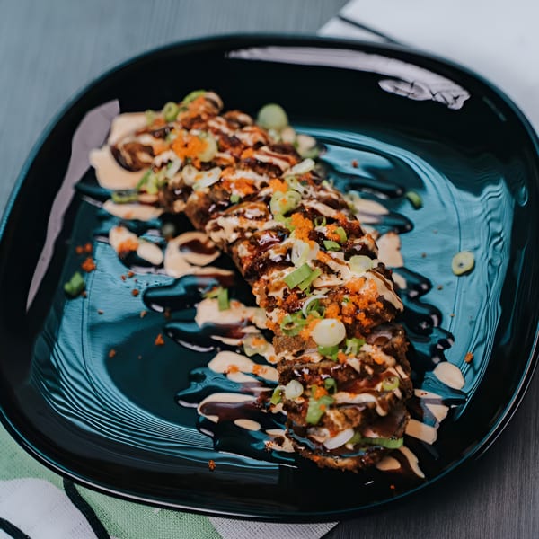 Crispy Vietnamese fusion rolls drizzled with sauces, topped with green onions and orange roe on a black plate.