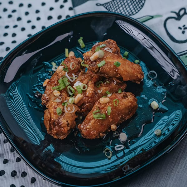 Crispy Vietnamese chicken wings, glazed and topped with chopped green onions and peanuts on a dark plate.